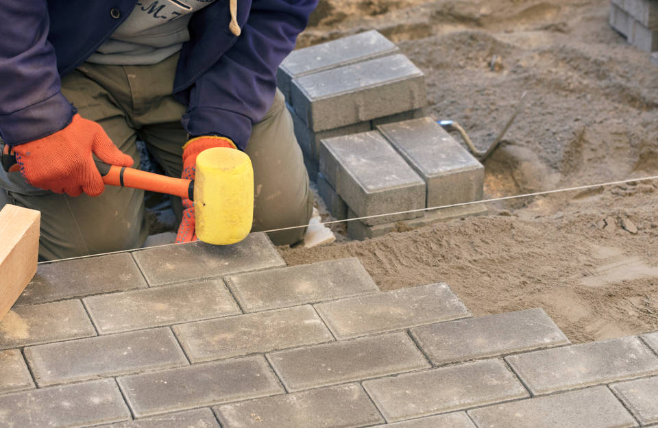 Person setting pavers evenly into sand base during a patio installation